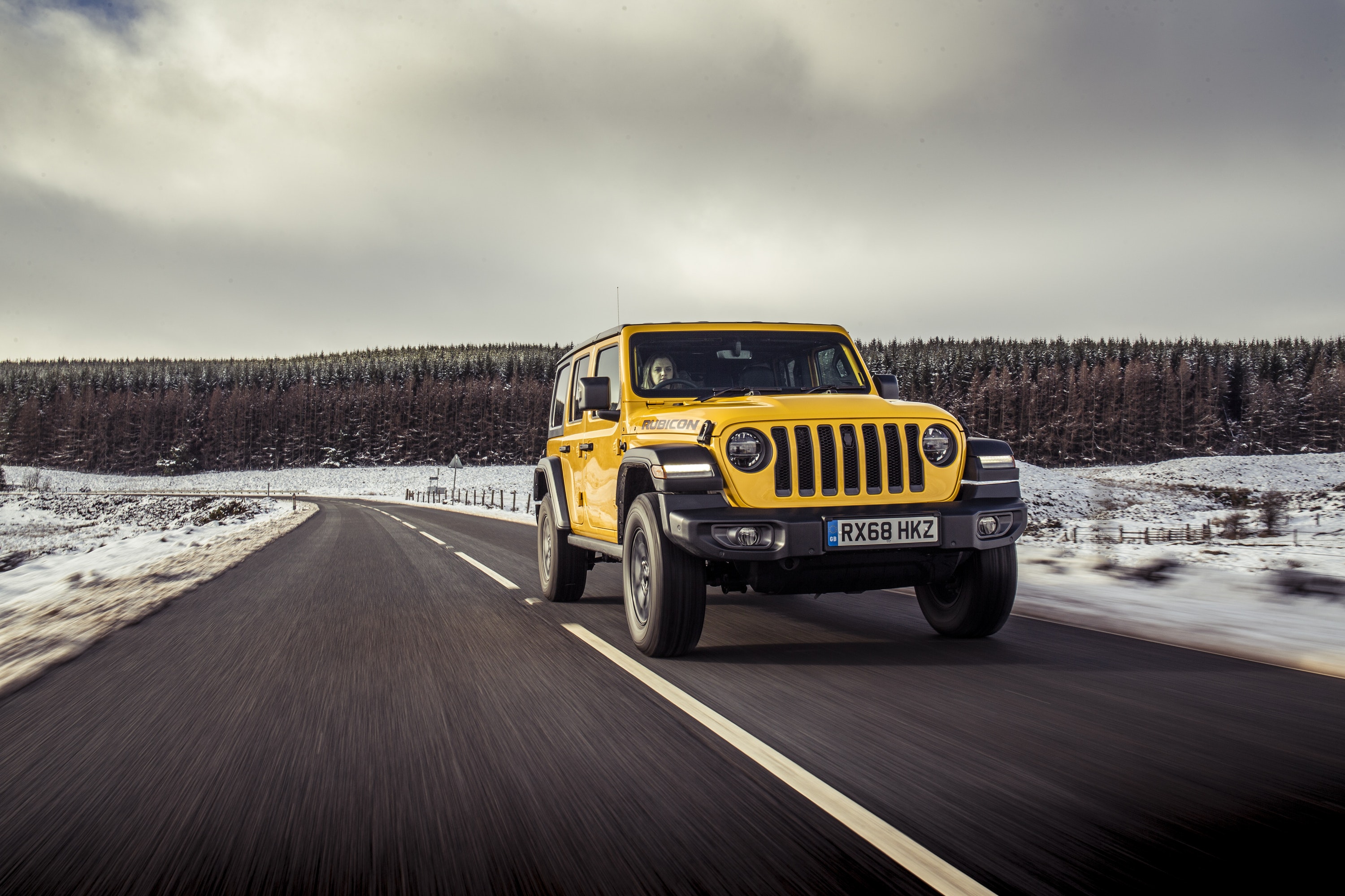 front view of yellow Jeep Wrangler driving on a road
